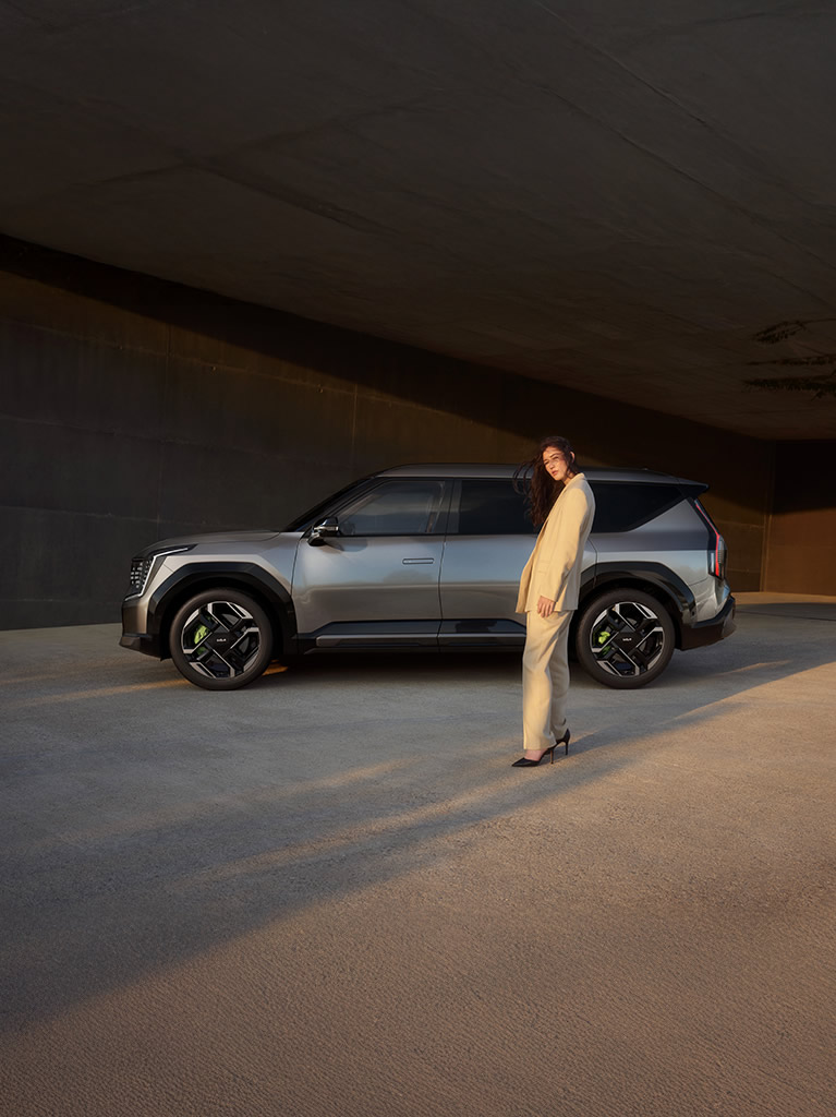 Kia EV9 GT, grau, Seitenansicht Fahrerseite, Frau steht auf Höhe der hinteren Tür