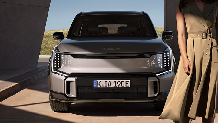 Kia EV9 GT, grau, Frontansicht, LED-Lichtsignatur, Frau steht auf Fahrerseite